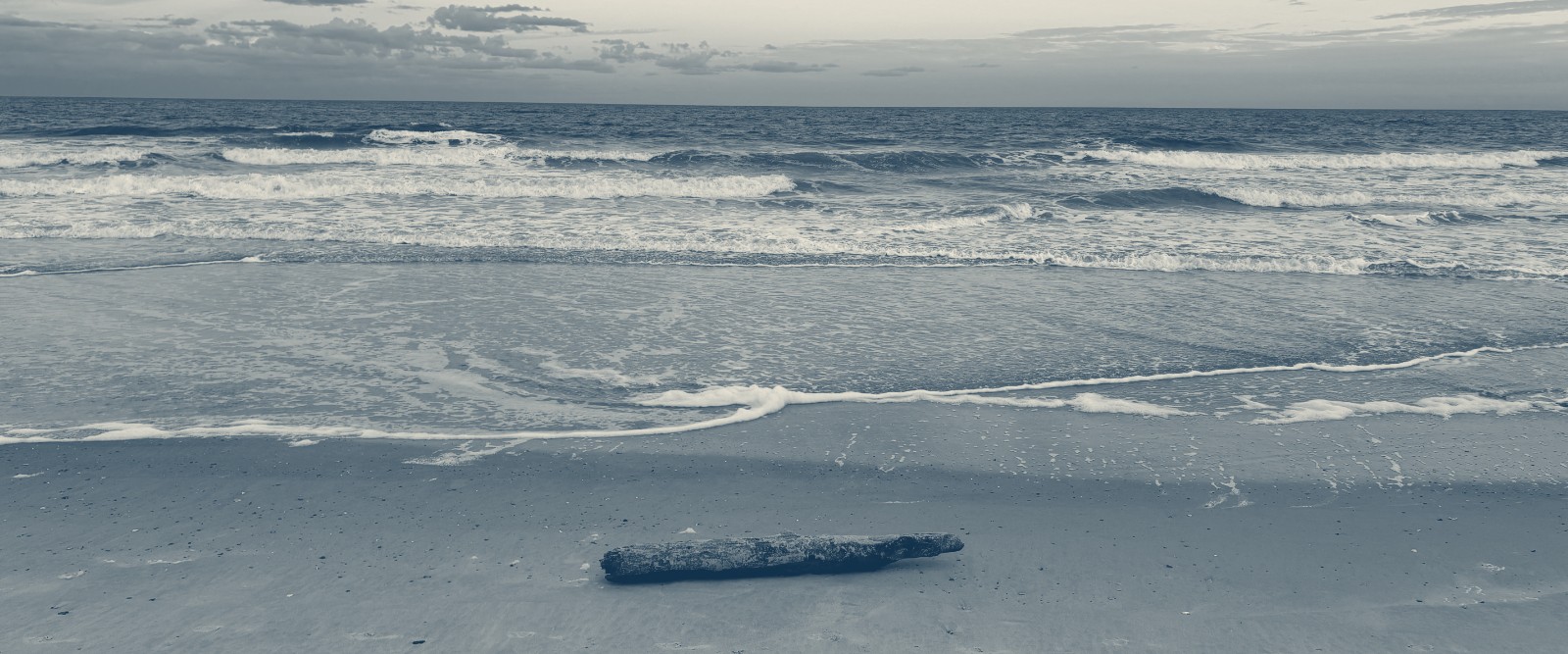 Main Beach at sunset, surf running up the sand and a driftwood log left by the tide